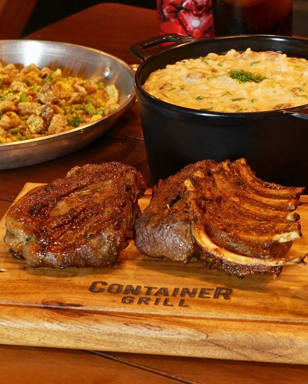 Costela e carneiro assados sobre tábua Container Grill, ao lado de farofa e baião cremoso