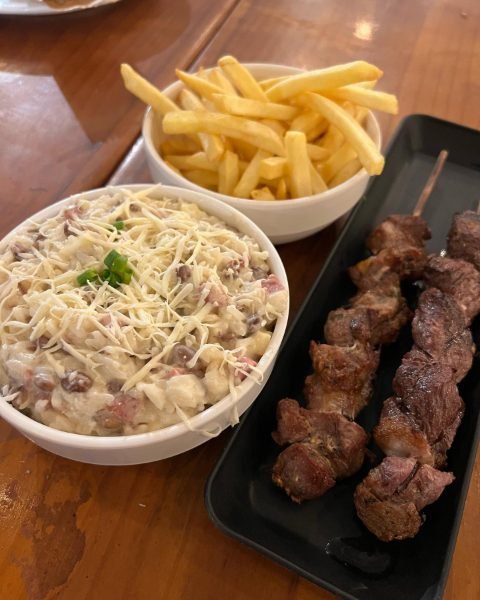 Espetinhos, baião cremoso e batata frita servidos na mesa