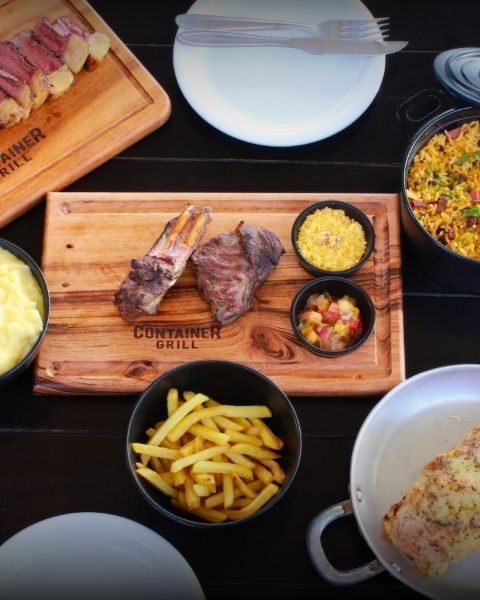 Mesa vista de cima com tábua de carnes, farofa, batata frita e acompanhamentos