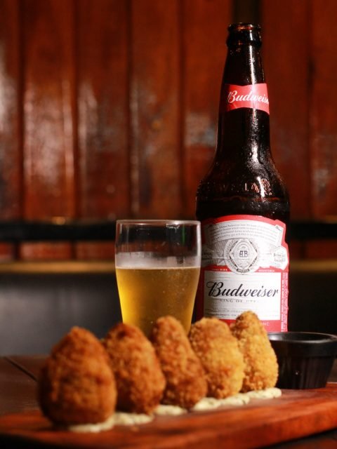 Croquetes na tábua ao lado de cerveja servida no copo