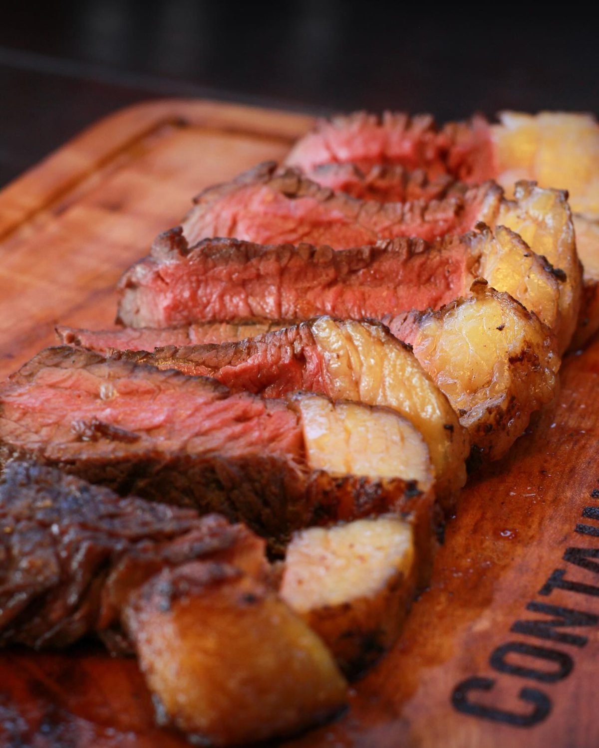 Picanha fatiada, com a capa de gordura dourada, sobre tábua marcada a fogo com a marca Container Grill